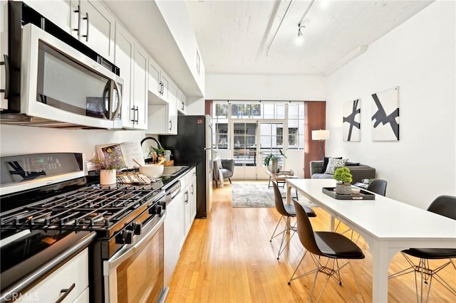 kitchen with appliances with stainless steel finishes, a breakfast bar, a sink, light wood-style flooring, and open floor plan