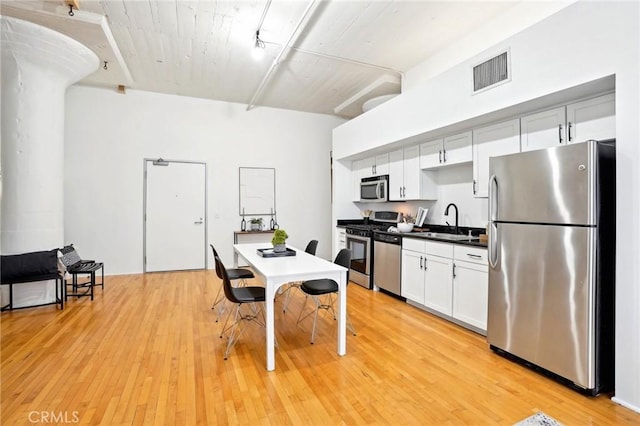kitchen featuring appliances with stainless steel finishes, a sink, dark countertops, light wood-style floors, and white cabinets