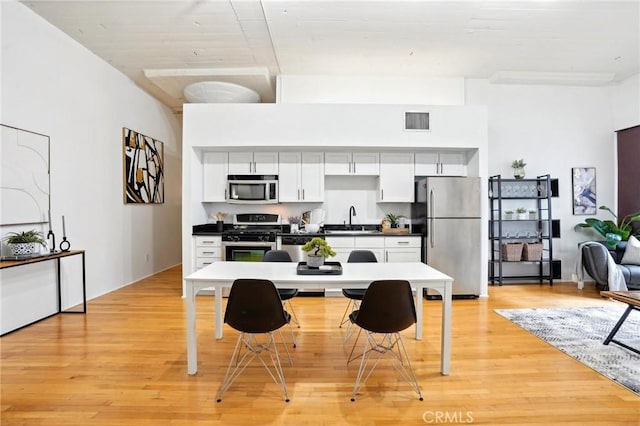 kitchen featuring appliances with stainless steel finishes, a sink, light wood finished floors, white cabinetry, and dark countertops