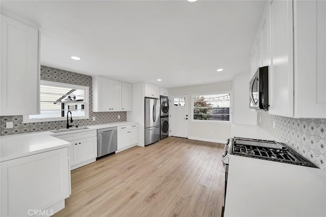 212 La Paloma, San Clemente, CA 92672 - kitchen featuring appliances with stainless steel finishes, estacked washer and dryer, a sink, light wood-type flooring, and white cabinets