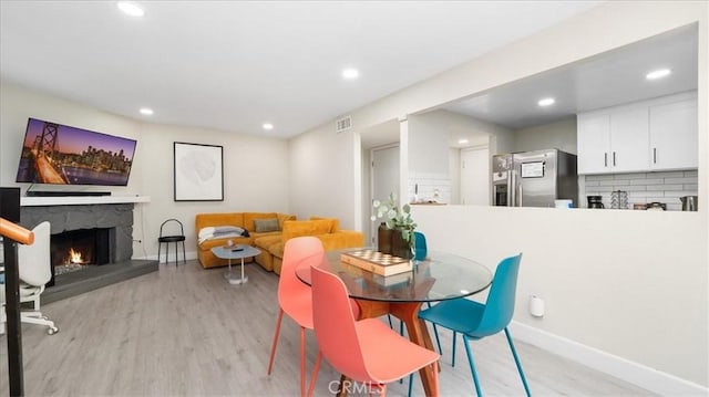 dining room featuring a fireplace, light wood-style floors, baseboards, and recessed lighting