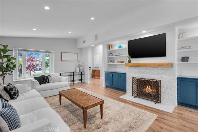 living room with a stone fireplace, light wood-style flooring, built in shelves, recessed lighting, and vaulted ceiling