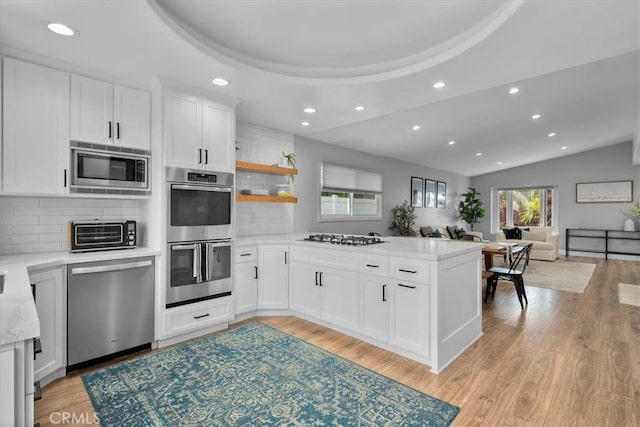 kitchen featuring appliances with stainless steel finishes, recessed lighting, a peninsula, backsplash, and open floor plan
