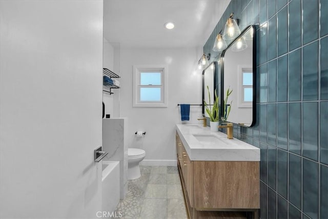 bathroom featuring toilet, baseboards, double vanity, tile patterned floors, and a tub to relax in