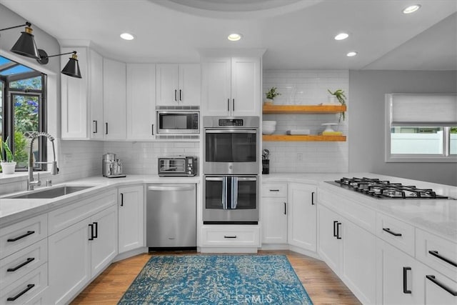 kitchen with appliances with stainless steel finishes, a sink, light wood-style floors, recessed lighting, and white cabinetry