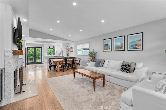 living area featuring lofted ceiling, light wood-style flooring, recessed lighting, and a stone fireplace