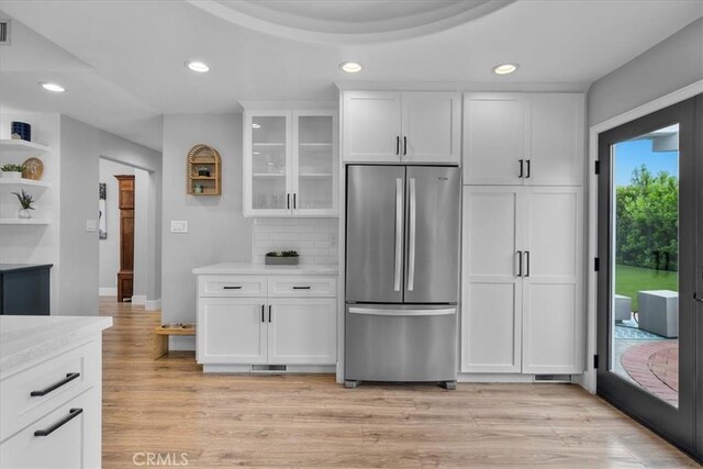 kitchen featuring freestanding refrigerator, white cabinets, backsplash, glass insert cabinets, and light wood-style flooring