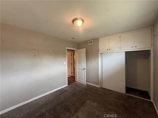 unfurnished bedroom with baseboards, dark carpet, and a closet