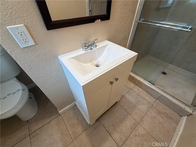 full bath with a textured wall, a shower stall, vanity, tile patterned floors, and toilet