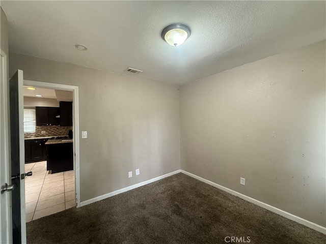 empty room with a textured ceiling, baseboards, and carpet flooring
