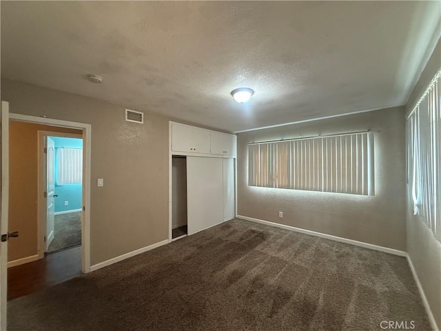 unfurnished bedroom featuring dark carpet, a closet, a textured ceiling, and baseboards