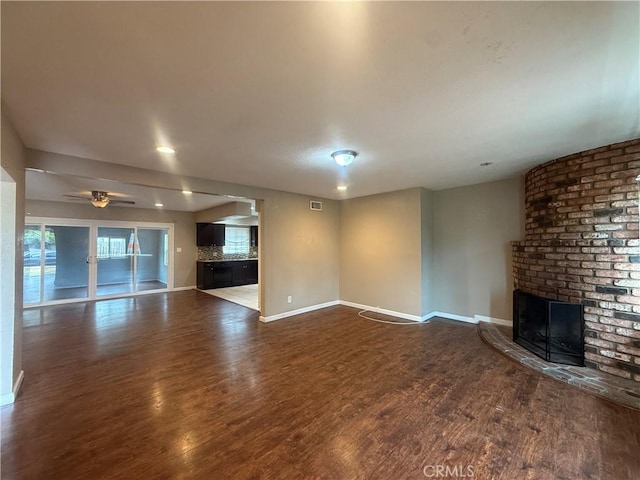 unfurnished living room featuring a brick fireplace, baseboards, dark wood-style floors, and ceiling fan