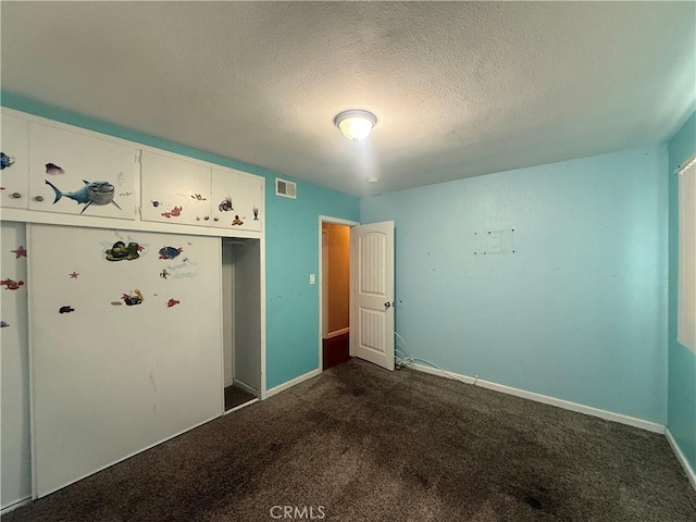 unfurnished bedroom featuring dark colored carpet, a textured ceiling, and baseboards