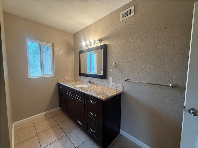 bathroom featuring vanity, tile patterned flooring, baseboards, and a textured wall