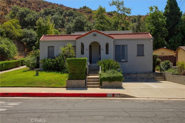 mediterranean / spanish-style home featuring a front yard, stucco siding, stairs, and a wooded view