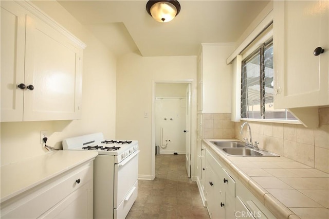 kitchen featuring white range with gas cooktop, a sink, white cabinets, tasteful backsplash, and tile countertops