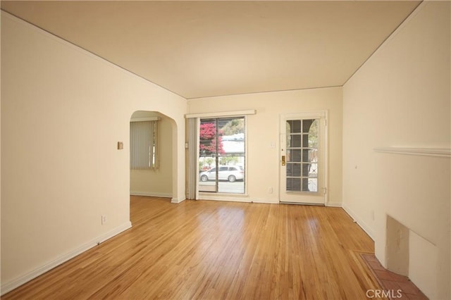 empty room with arched walkways, light wood-type flooring, and baseboards