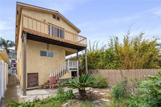 back of property with stucco siding, fence, and stairs