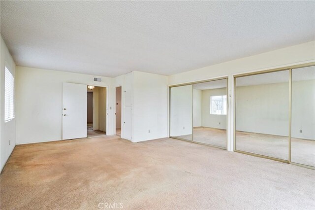 unfurnished bedroom with two closets, carpet floors, and a textured ceiling