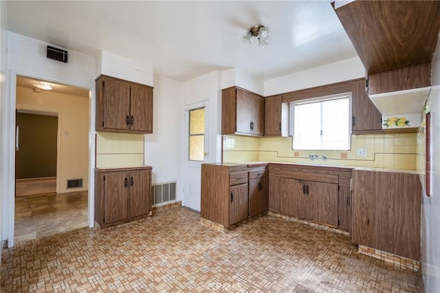 kitchen with open shelves, light countertops, tasteful backsplash, and brown cabinetry