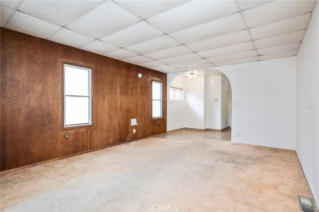 spare room featuring arched walkways, wooden walls, carpet flooring, and a paneled ceiling