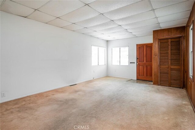 carpeted empty room with a drop ceiling and baseboards