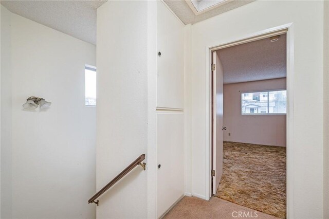hall with light colored carpet, an upstairs landing, and a textured ceiling
