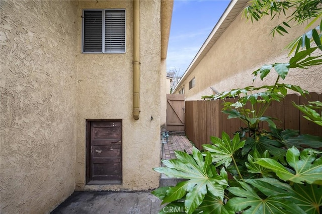 property entrance with stucco siding, fence, and a gate