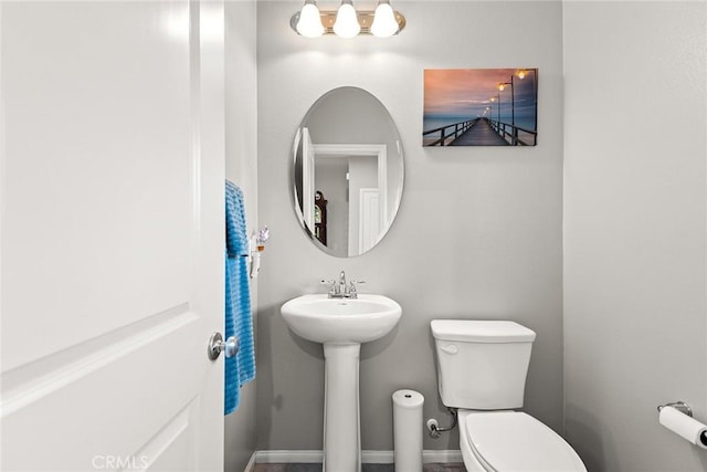half bathroom featuring toilet, a sink, and baseboards