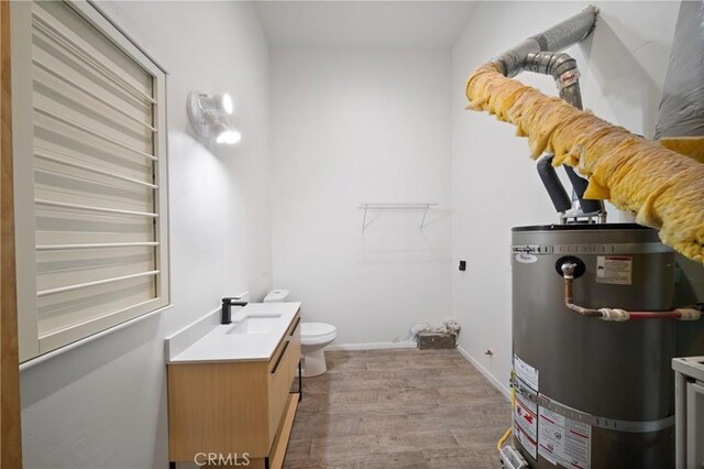 bathroom featuring strapped water heater, vanity, wood finished floors, toilet, and baseboards