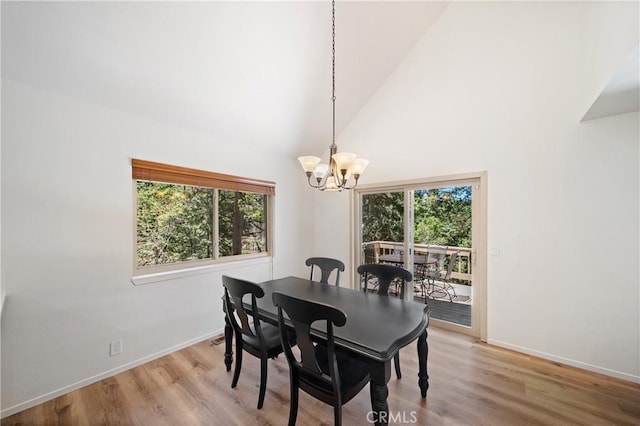 dining room with plenty of natural light, a chandelier, baseboards, wood finished floors, and a towering ceiling