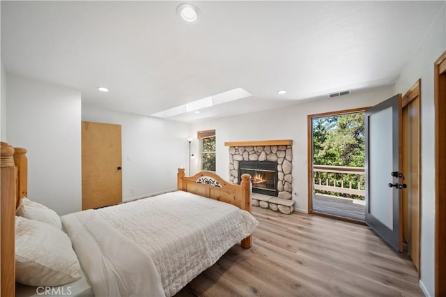 bedroom featuring a skylight, multiple windows, a fireplace, wood finished floors, and recessed lighting