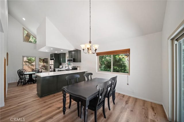 dining space with a chandelier, plenty of natural light, light wood-style flooring, and high vaulted ceiling
