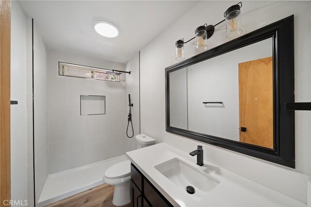 bathroom with toilet, a tile shower, vanity, and wood finished floors