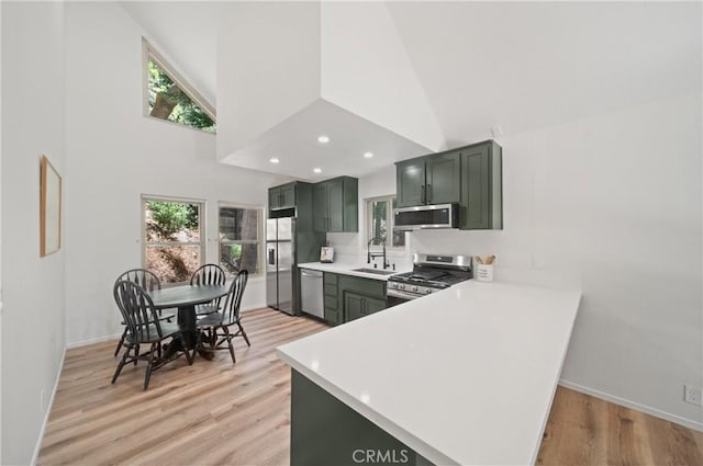 kitchen featuring appliances with stainless steel finishes, green cabinetry, a sink, light countertops, and light wood-style flooring
