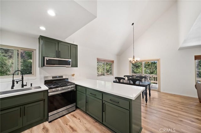 kitchen with green cabinetry, appliances with stainless steel finishes, a sink, a peninsula, and light countertops
