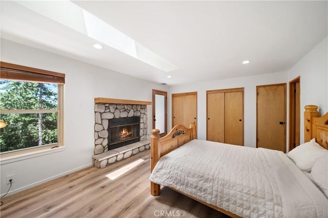bedroom with a skylight, recessed lighting, two closets, light wood-style flooring, and baseboards