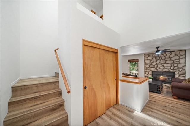 stairway with wood finished floors, a ceiling fan, a stone fireplace, and a towering ceiling