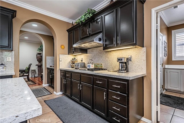 kitchen with under cabinet range hood, ornamental molding, arched walkways, light tile patterned floors, and stainless steel gas cooktop