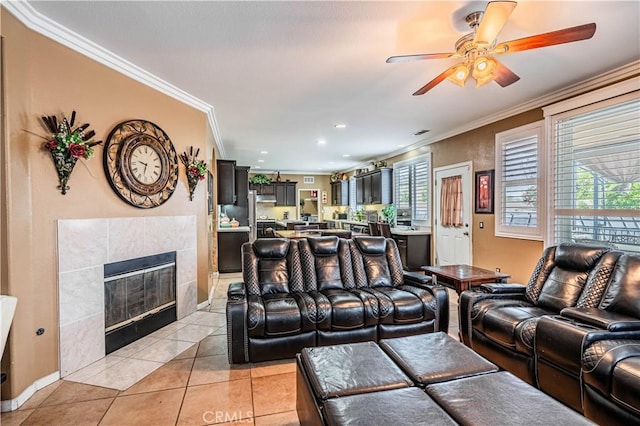living room featuring crown molding, healthy amount of natural light, a fireplace, a ceiling fan, and light tile patterned flooring
