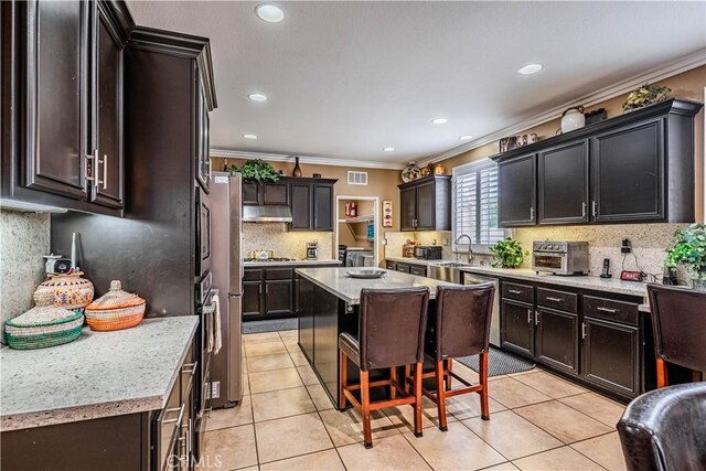 kitchen featuring ornamental molding, a sink, decorative backsplash, under cabinet range hood, and light tile patterned floors