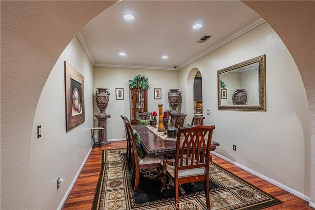 dining area with arched walkways, wood finished floors, crown molding, recessed lighting, and baseboards