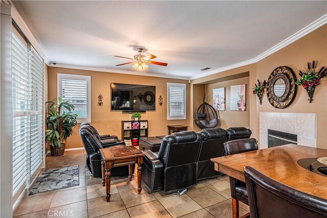 living area featuring a tile fireplace, ceiling fan, light tile patterned floors, and ornamental molding
