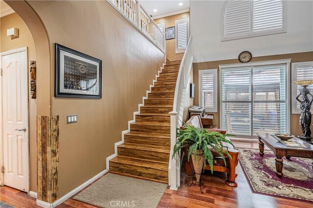 staircase featuring wood finished floors, arched walkways, baseboards, and a high ceiling