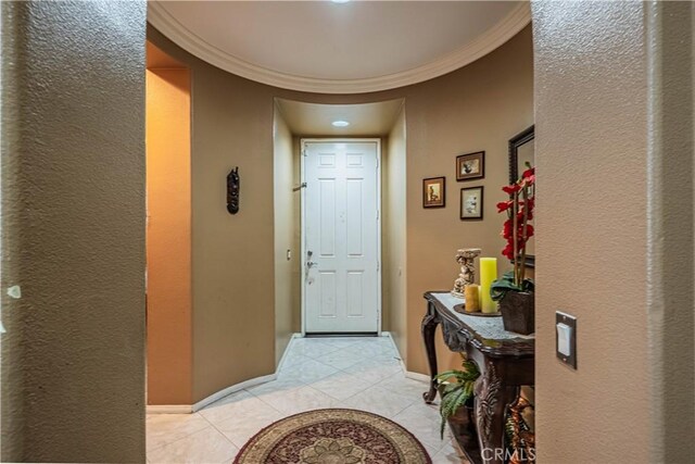 entryway featuring light tile patterned floors, crown molding, a textured wall, and baseboards
