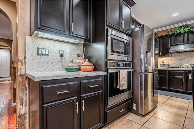 kitchen featuring appliances with stainless steel finishes, crown molding, tasteful backsplash, arched walkways, and under cabinet range hood