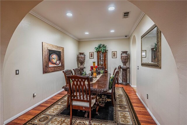 dining space with arched walkways, wood finished floors, crown molding, recessed lighting, and baseboards