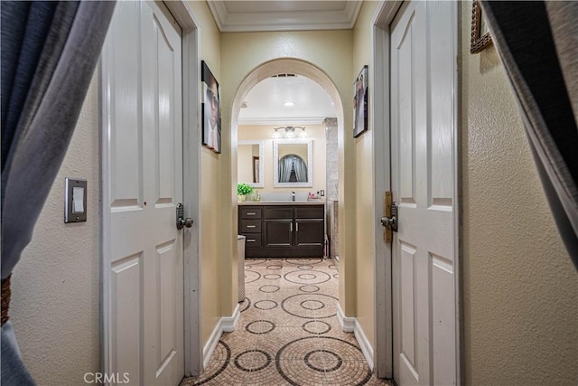 corridor featuring ornamental molding, a sink, arched walkways, baseboards, and a textured wall