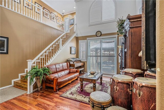 living area with stairs, wood finished floors, a high ceiling, and baseboards