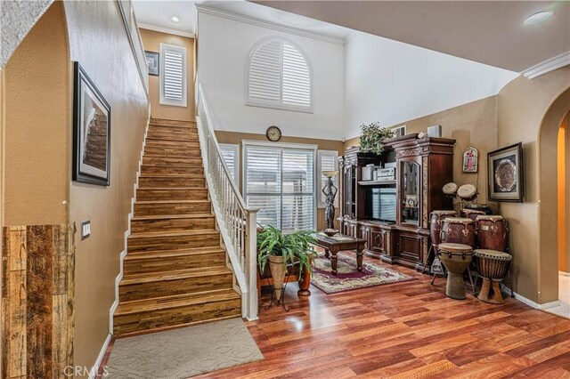 stairway featuring arched walkways, ornamental molding, wood finished floors, a high ceiling, and recessed lighting